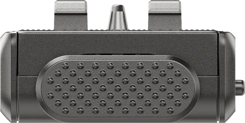 Ein dunkelgraues rechteckiges Gerät mit strukturierter Oberfläche und kreisförmigen Erhebungen. Zwei erhöhte Abschnitte und ein zentraler Knopf sind sichtbar.