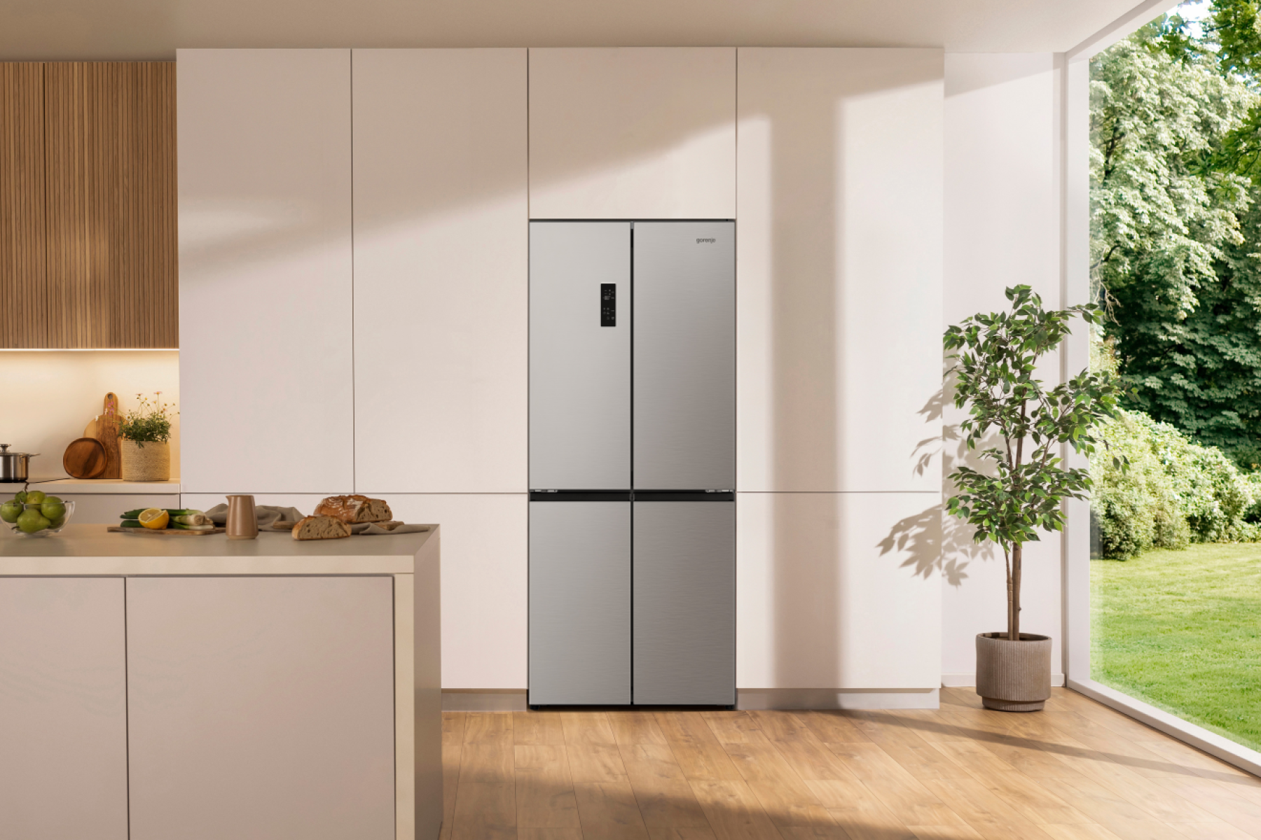 Moderne Küche mit silbernem Kühlschrank, Theke mit Essen und Pflanze neben einem großen Fenster mit Gartenblick.