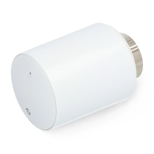 Białe cylindryczne urządzenie ze srebrną górą. Prawdopodobnie inteligentny termostat domowy, ustawiony pod kątem na białej powierzchni.