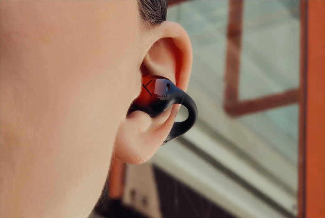 Gros plan sur une oreille avec un écouteur noir et rouge inséré. L'écouteur est partiellement dans l'oreille.