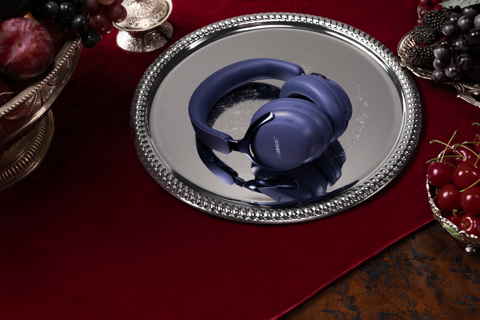 Casque Bose bleu sur un plateau argenté, entouré de fruits sur une surface rouge.