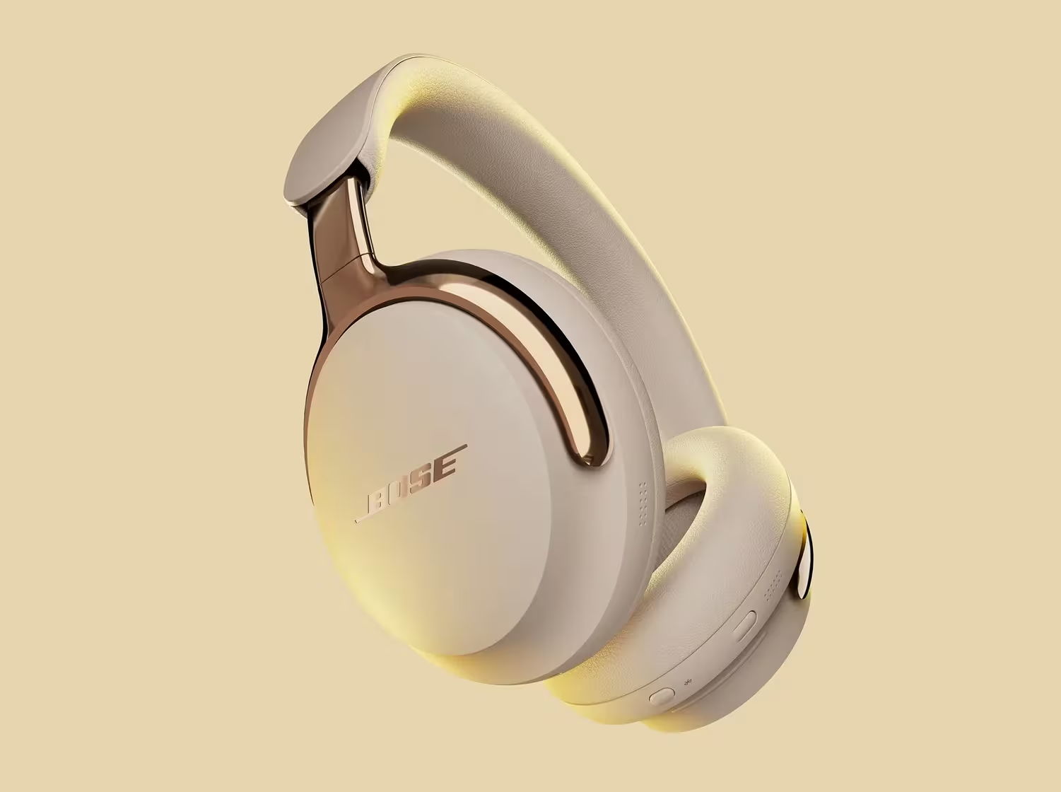 Cuffie Bose color crema con dettagli dorati, su sfondo giallo chiaro. Il logo Bose è visibile.