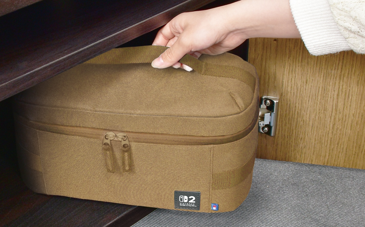 Una mano tira fuori una borsa marrone da un armadio. La borsa ha una cerniera, un manico e un logo Nintendo Switch.