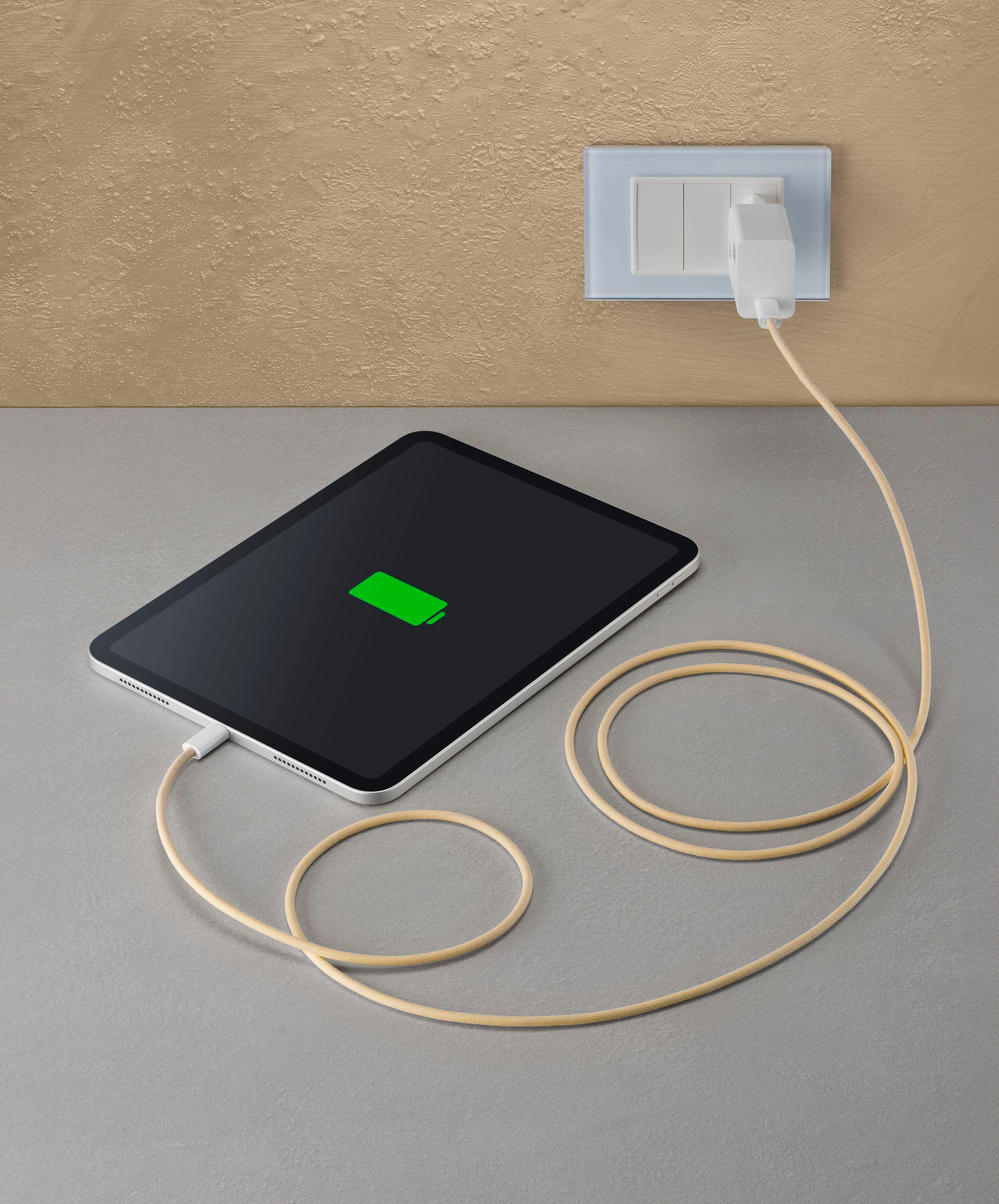 Tablet wird aufgeladen mit grünem Akkusymbol. Ladegerät in der Wand. Beiges Kabel auf grauer Oberfläche.