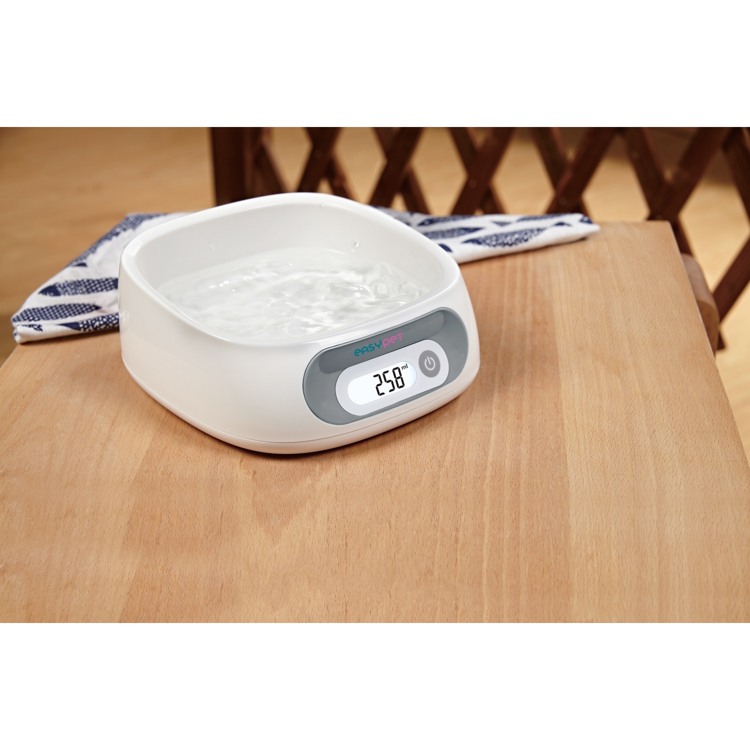 A white water bath with digital display, reading 258, sits on a wooden table. A patterned cloth and a wooden chair are in the background.