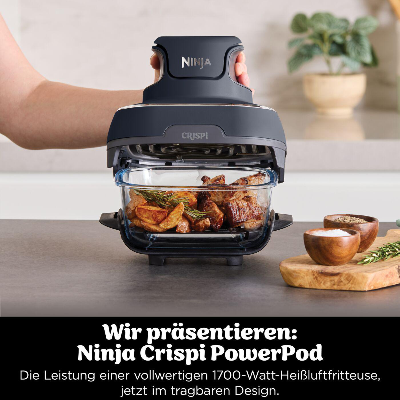 Ninja Crispi PowerPod Heißluftfritteuse mit gekochten Speisen. Hand hält die Oberseite. Gewürze daneben.