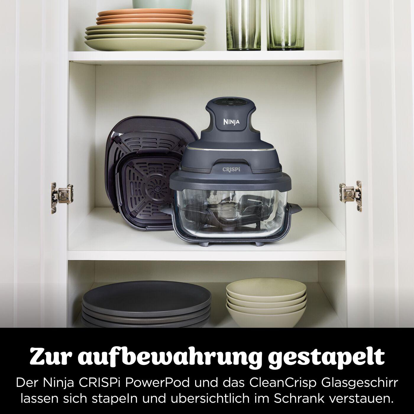 Ninja Crispi PowerPod und Zubehör sind in einem Schrank mit Tellern und Gläsern auf Regalen gestapelt.