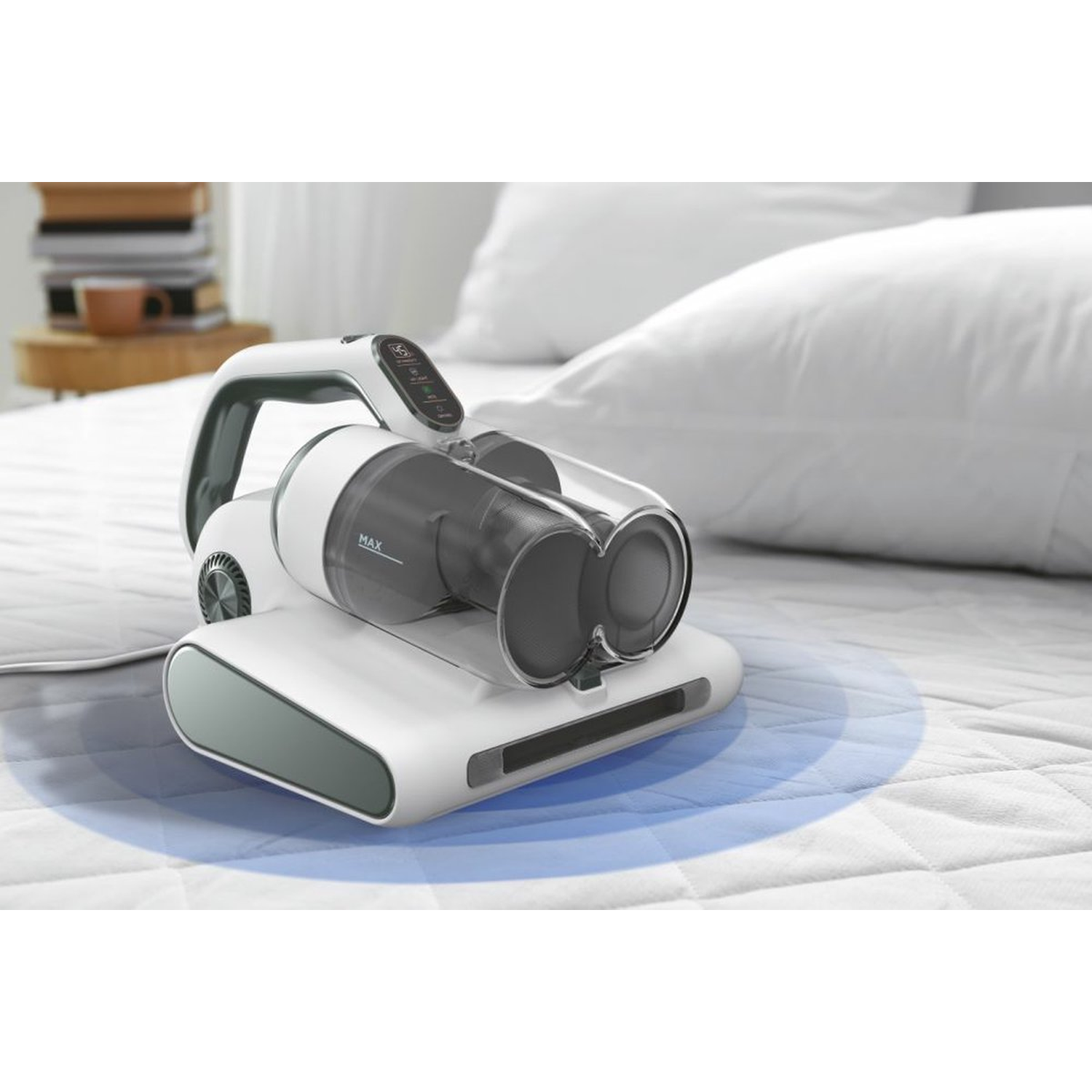 A white and gray cordless vacuum cleaner on a bed. There is a pillow in the background. A stack of books is visible.