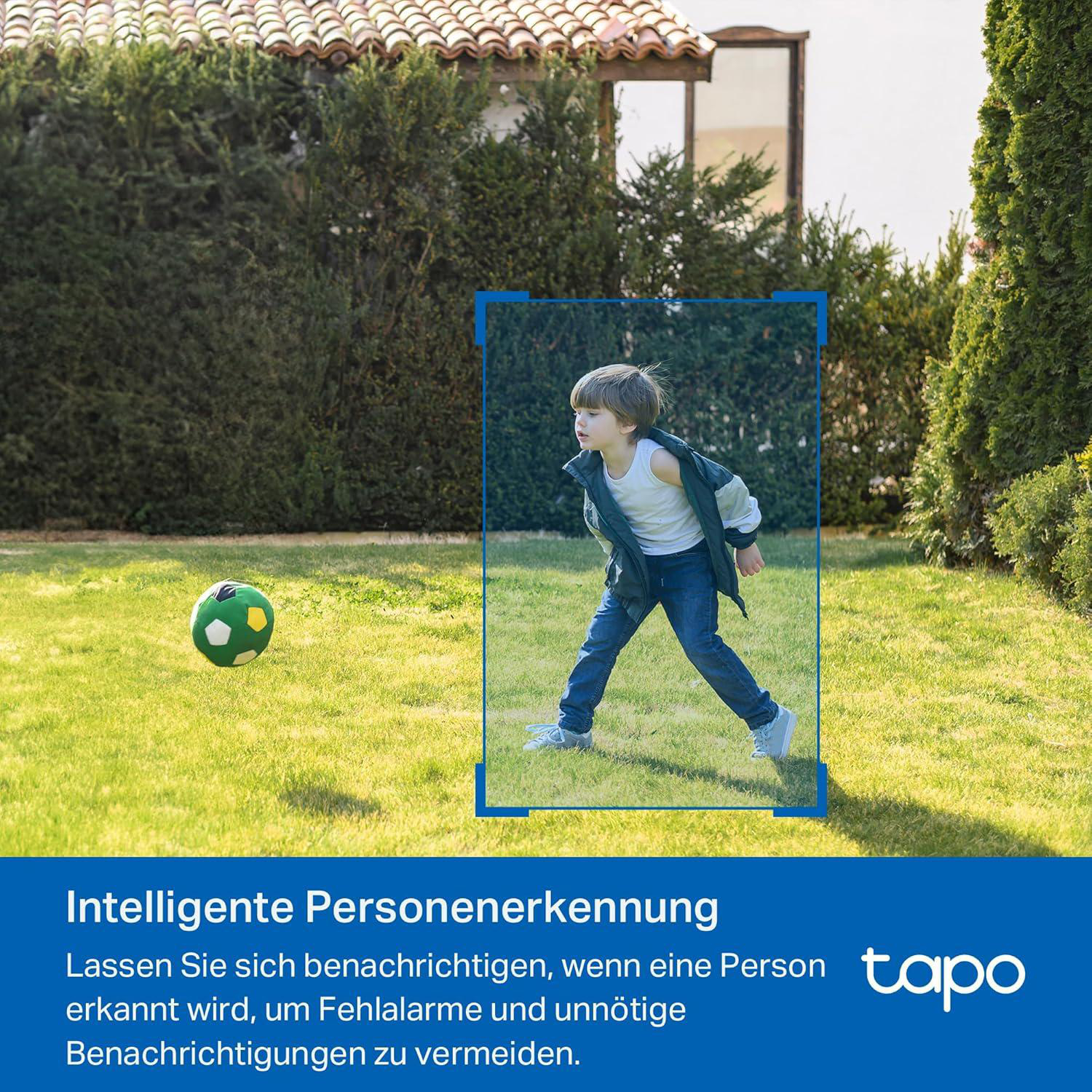 Ein Junge in Jeans rennt auf Gras, ein grün-weißer Ball in der Nähe. Grüne Büsche und ein Haus sind im Hintergrund.