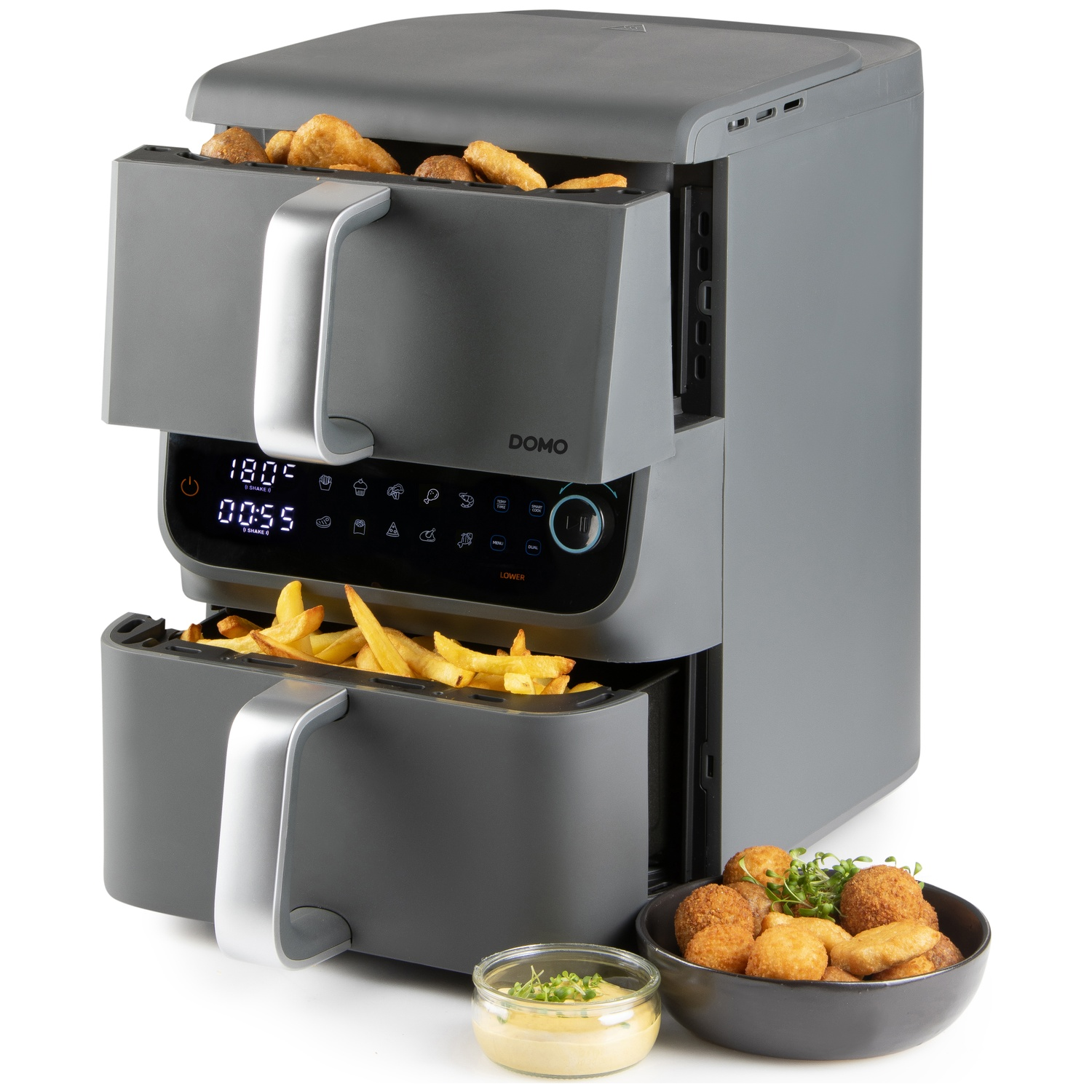 Une friteuse à air double avec de la nourriture à l'intérieur, un bol d'aliments frits et une petite coupelle de sauce.