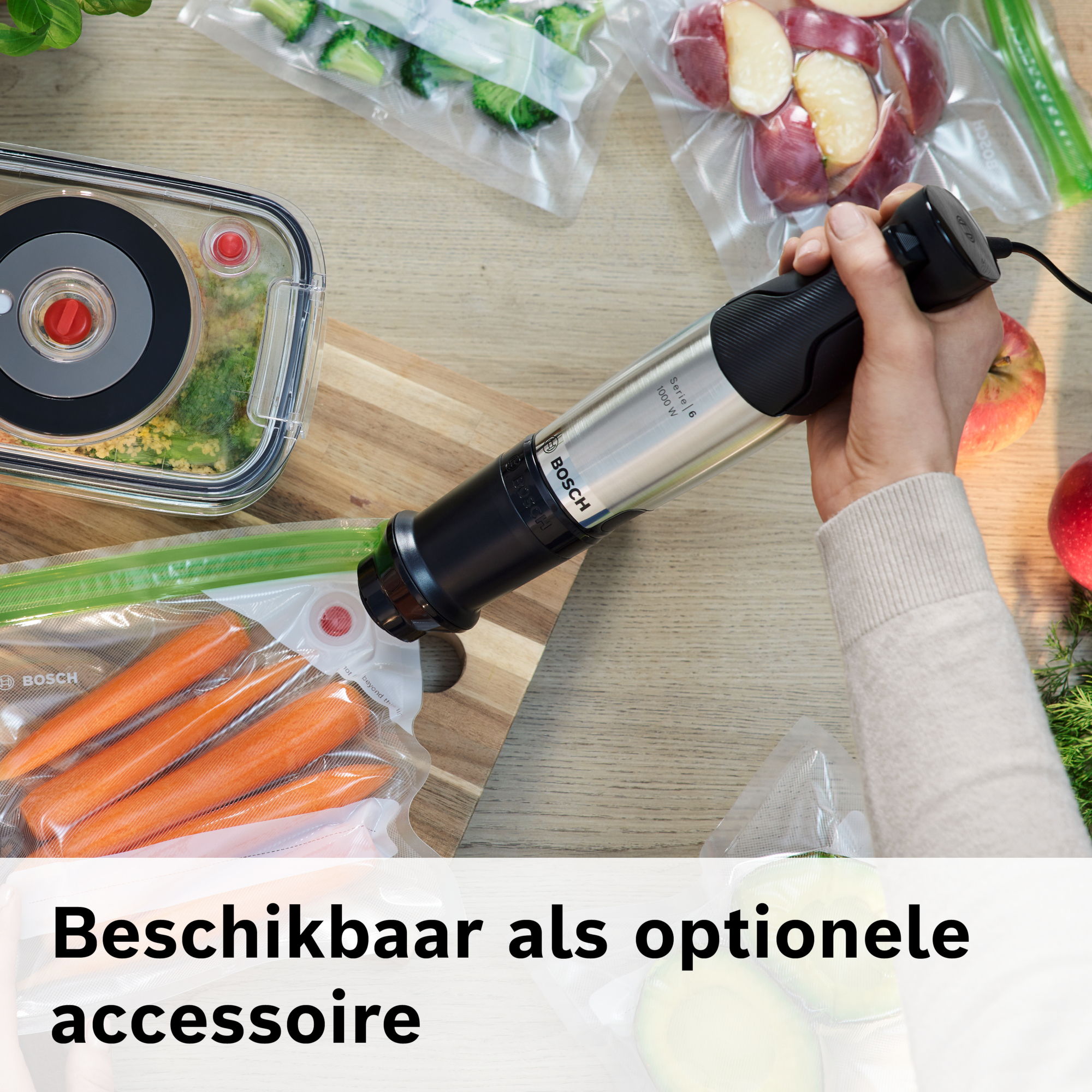 Hand die een Bosch staafmixer vasthoudt. Groenten en fruit zijn vacuüm verpakt. Tekst: Verkrijgbaar als optioneel accessoire.