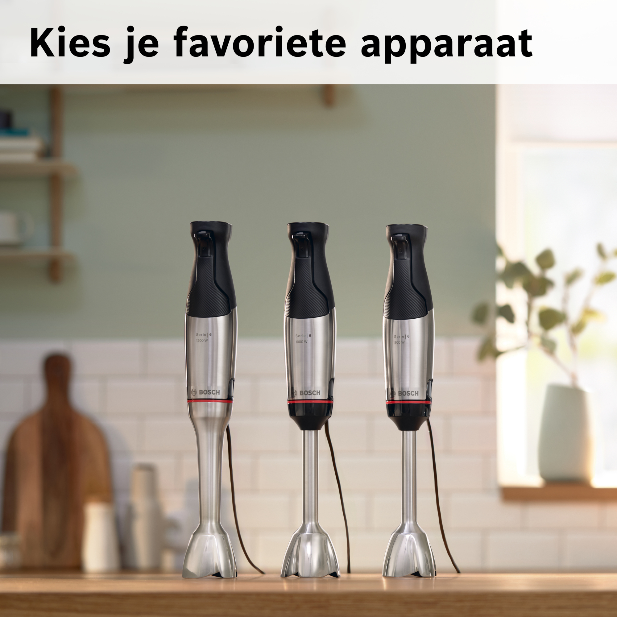 Drie Bosch staafmixers op een houten oppervlak. Ze hebben zwarte bovenkanten en zilveren behuizingen. Achtergrond is een raam en planten.