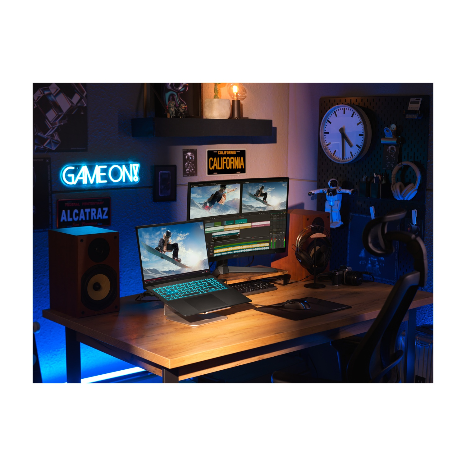 Un'impostazione di gioco con laptop, monitor e altoparlanti su una scrivania di legno. Un'insegna al neon 'Game On!' e un orologio a muro.