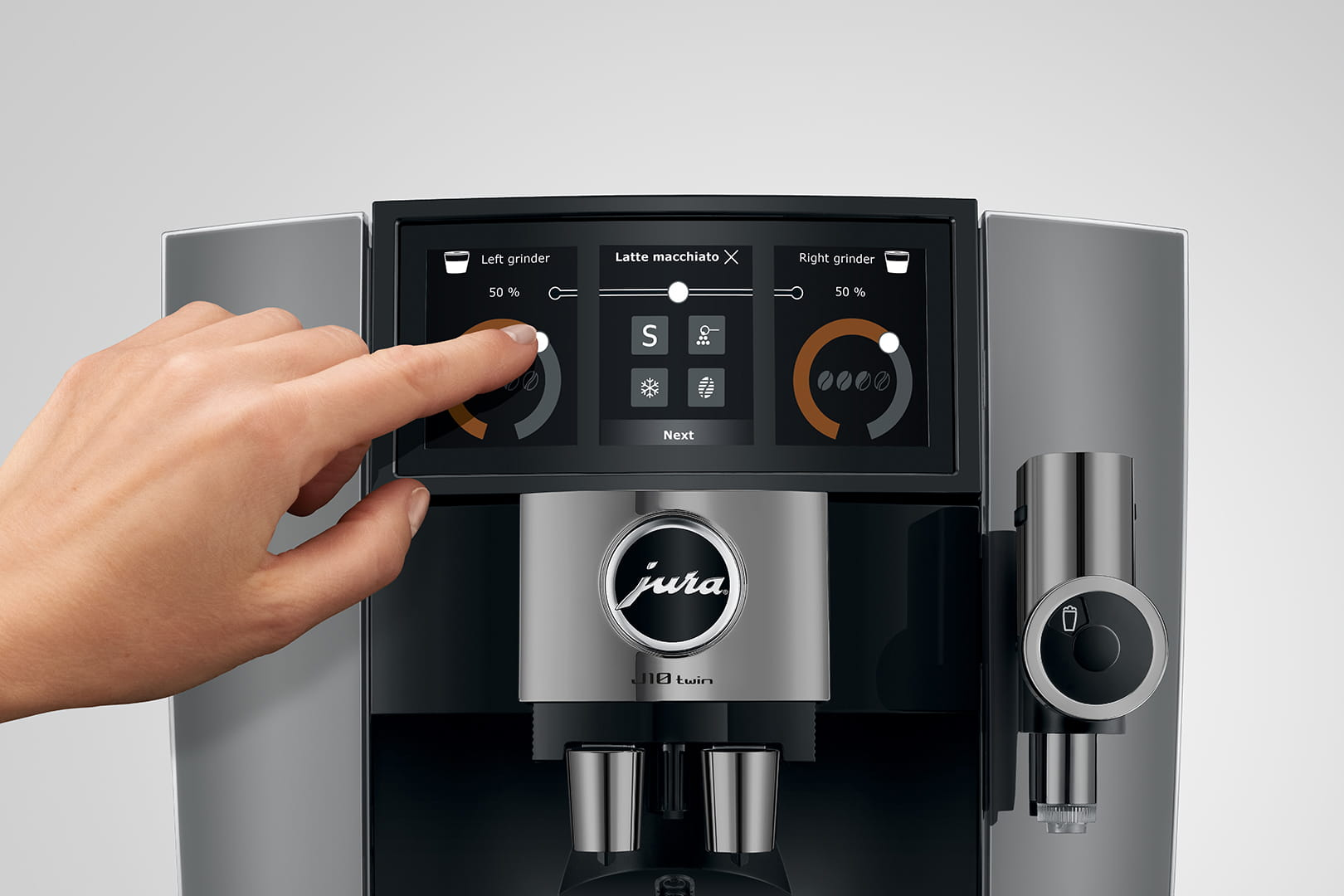 Eine Hand berührt den Bildschirm einer Kaffeemaschine. Es werden Mahleinstellungen und Getränkeoptionen angezeigt. Die Maschine hat ein Jura-Logo.