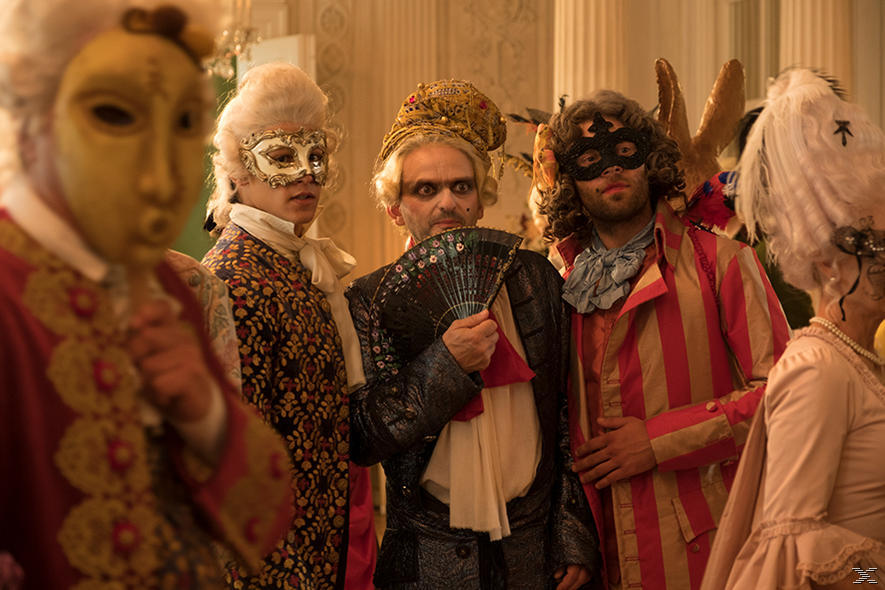 Gruppe von kostümierten Personen auf einem Maskenball. Masken, Perücken und aufwendige Kleidung. Einige halten einen Fächer.