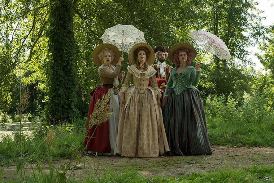 Fünf Personen in historischen Kostümen stehen in einem Park. Drei Frauen halten Sonnenschirme. Bäume umgeben sie. Die Szene ist im Freien.