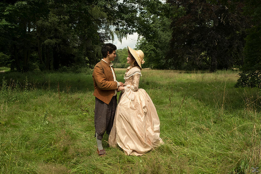 Ein Paar in historischer Kleidung steht auf einem Feld. Die Frau trägt ein großes Kleid und einen Hut, der Mann eine braune Jacke.