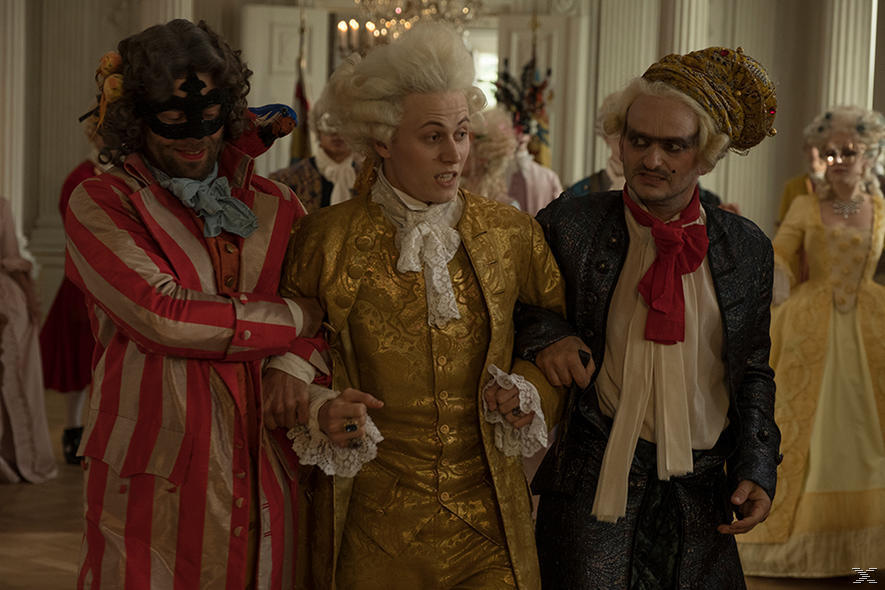Drei Männer in historischen Kostümen gehen zusammen. Einer trägt eine Maske, ein anderer einen goldenen Anzug, der dritte eine schwarze Jacke.