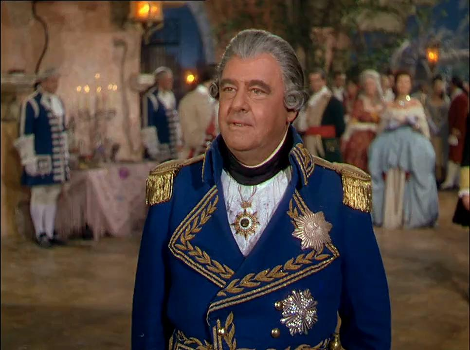 Mann in blauem Militärmantel mit Goldbesatz und Medaillen, blickt den Betrachter an. Andere Personen in historischen Kostümen im Hintergrund.