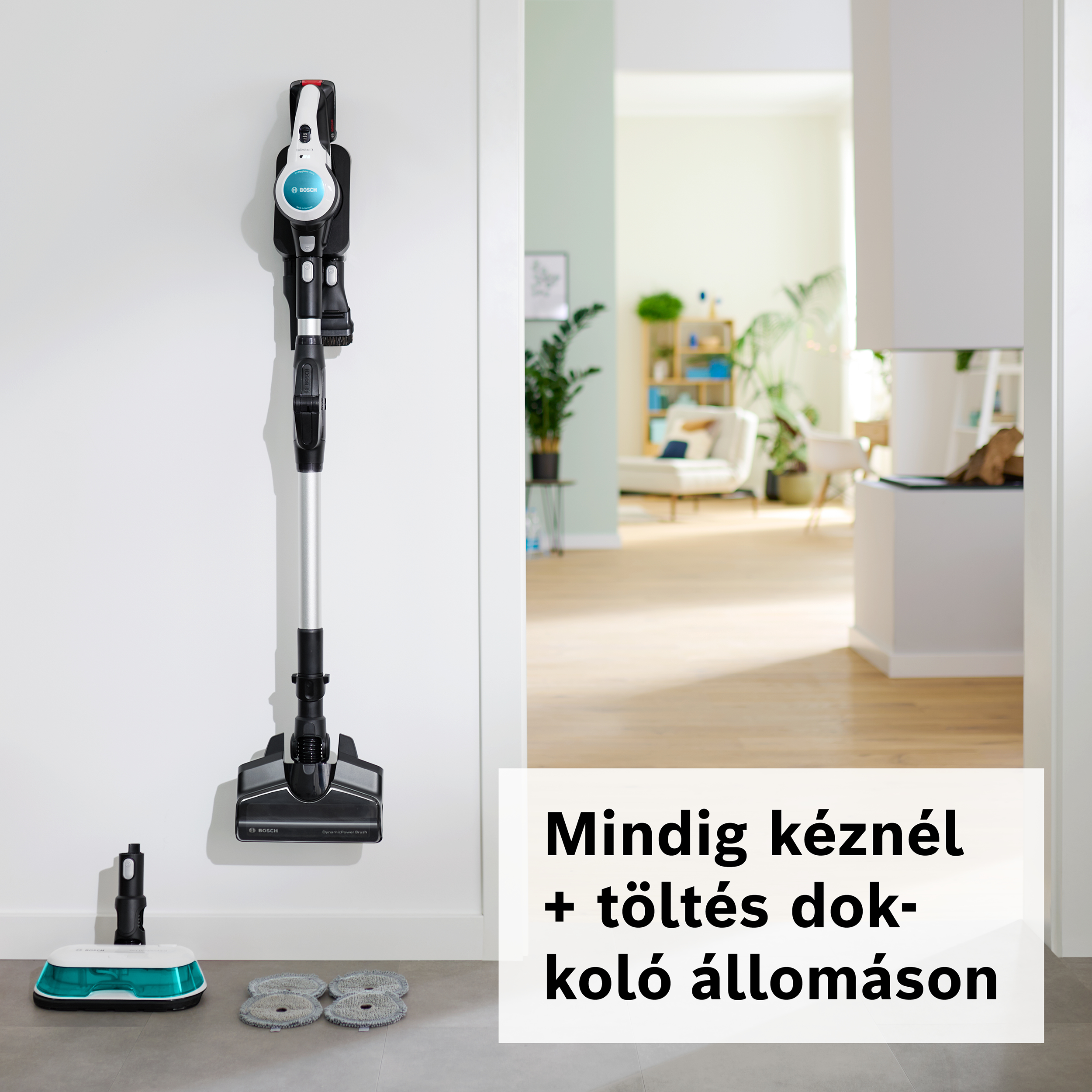 Egy fehér falon egy Bosch porszívó látható. Előtte padlótisztító és tisztítópárnák vannak. Egy szoba látható egy ajtón keresztül.
