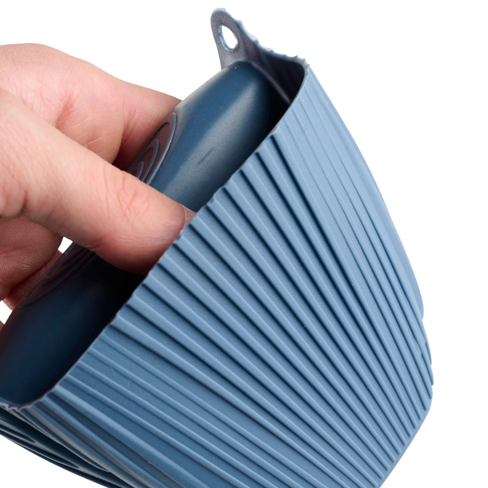 Una mano sostiene una funda de silicona azul y acanalada para taza. La funda tiene un pequeño agujero en la parte superior. El fondo es blanco.