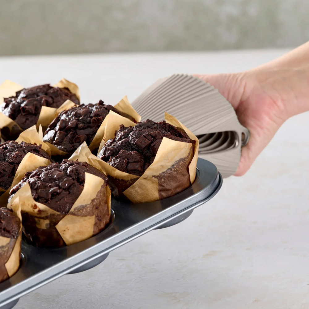 Una mano sostiene una bandeja para muffins con muffins de chocolate. Los muffins están en papel. El fondo está borroso.