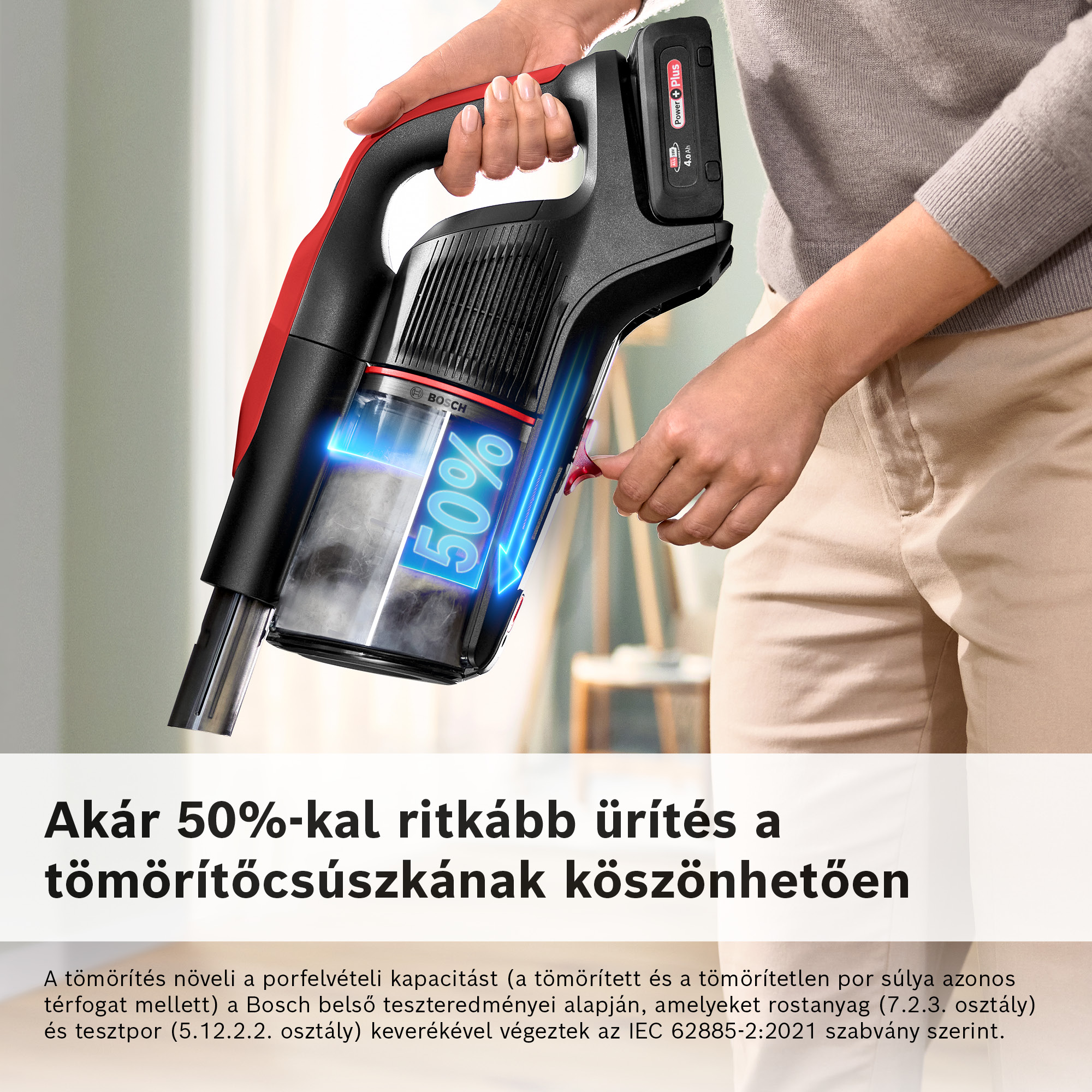 Egy személy egy fekete-piros porszívót tart. A porszívó átlátszó portartállyal és egy 50%-os grafikával rendelkezik.