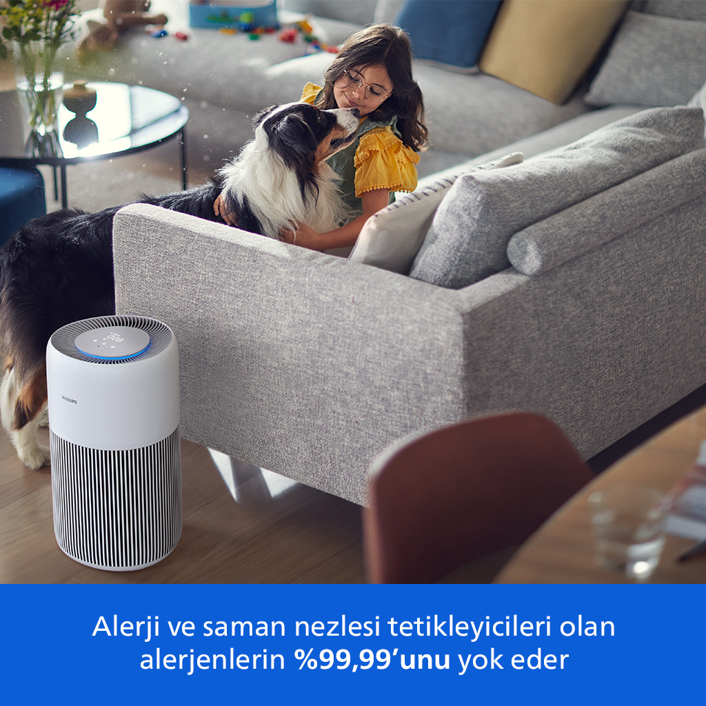 Gözlüklü bir kız, gri bir kanepede bir köpeği okşuyor. Ön planda bir hava temizleyici var. Altta metin.