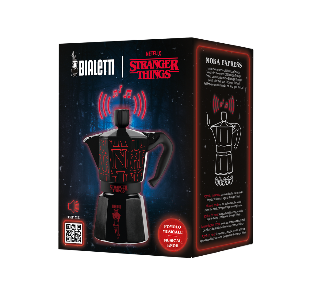 Schwarze Bialetti Moka-Kanne mit Stranger Things-Logo, musikalischem Knopf und roten Akzenten auf einer Themenbox.