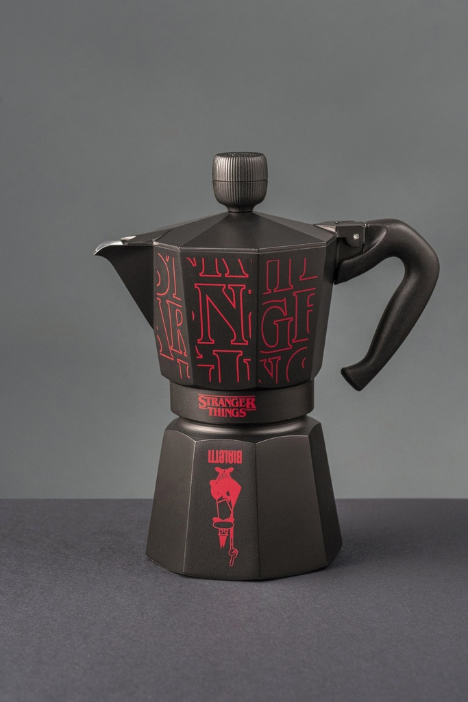Schwarzer Kaffeezubereiter mit rotem Stranger Things-Logo. Es steht auf einer dunkelgrauen Oberfläche vor grauem Hintergrund.