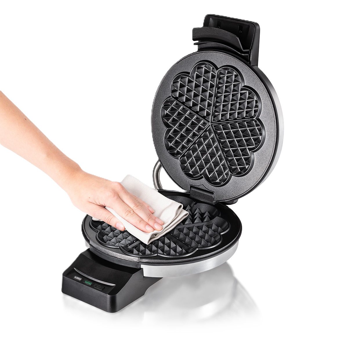 Eine Person reinigt ein Waffeleisen mit einem weißen Tuch. Das Eisen ist geöffnet und zeigt die Waffelgitter. Schwarzes und silbernes Gerät.