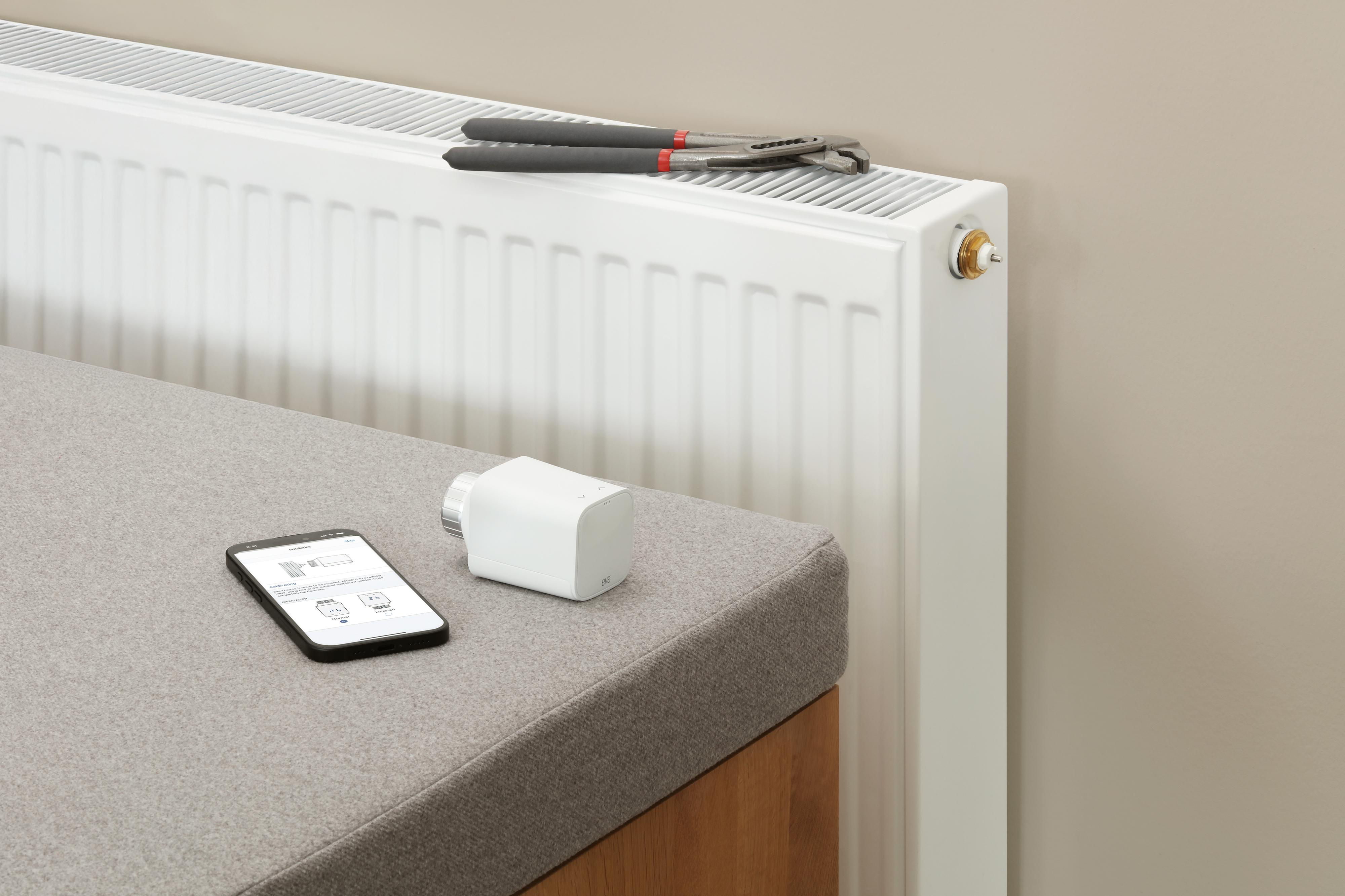 Ein Heizkörper mit einem Schraubenschlüssel, einem intelligenten Thermostat und einem Smartphone auf einer Bank.