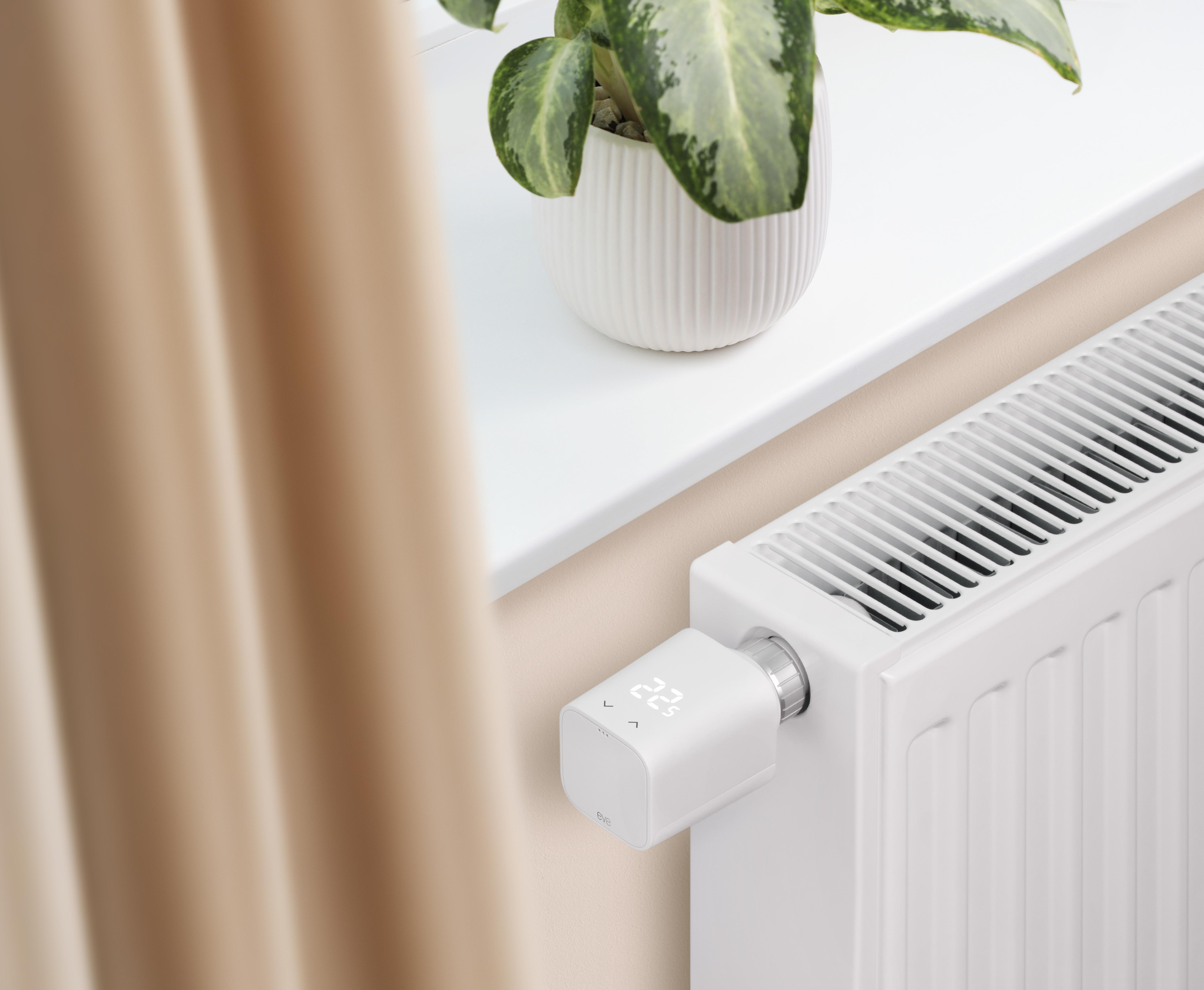 Ein weißer Heizkörper mit digitalem Thermostat, eine Pflanze auf der Fensterbank und ein beiger Vorhang.