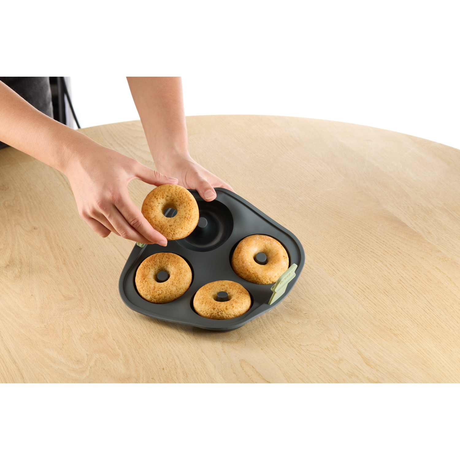 Hands placing a donut on a tray with others. The tray is on a wooden table.