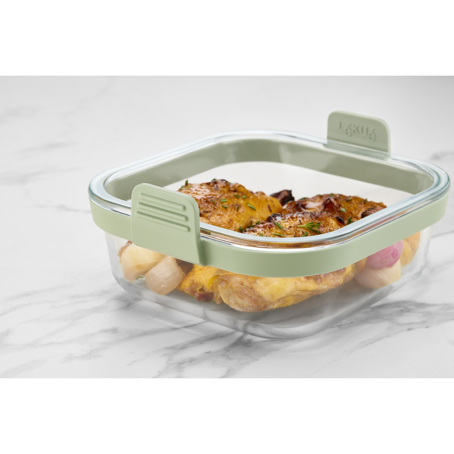 A clear glass food container with a light green lid. Inside, there's cooked chicken and some vegetables. The container rests on a marble surface.