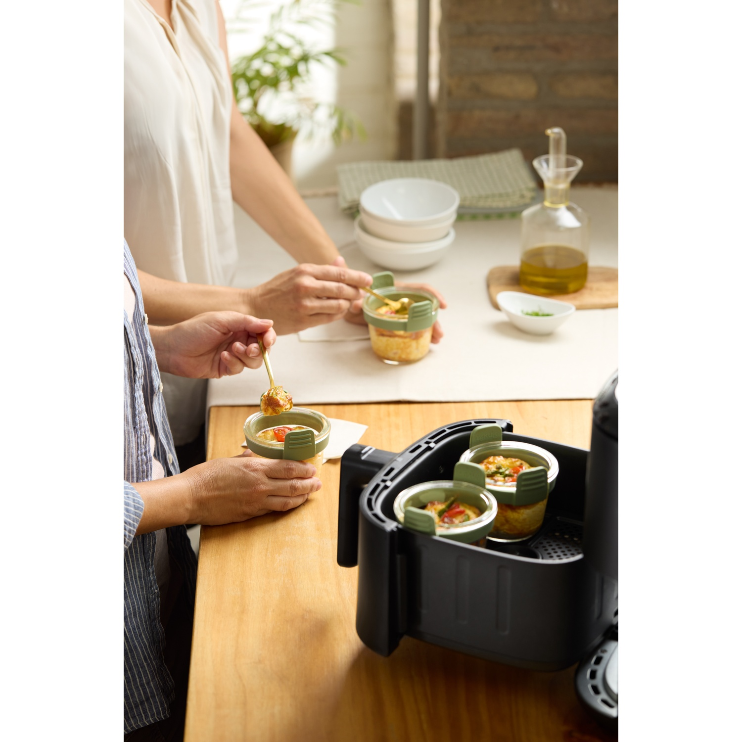 Twee mensen bereiden eten in een keuken. Voedselcontainers zitten in de airfryer. Andere ingrediënten liggen op de tafel.