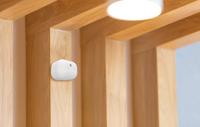 Białe urządzenie zamontowane na drewnianej ścianie. Tło to drewniane belki i miękkie światło sufitowe.