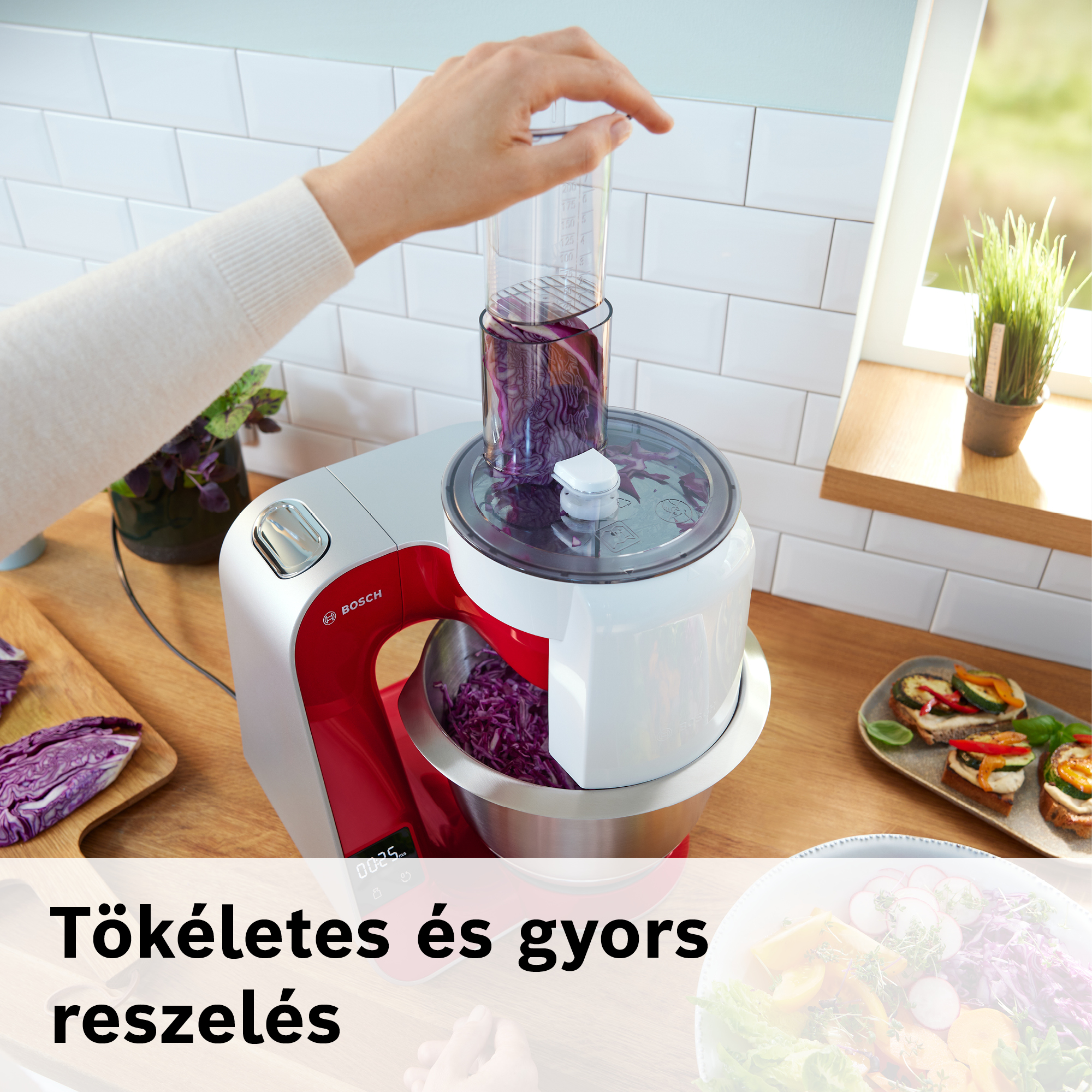 Egy kéz egy konyhai robotgépet használ, benne vörös káposztával. A gép fa pulton van. Étel készül.