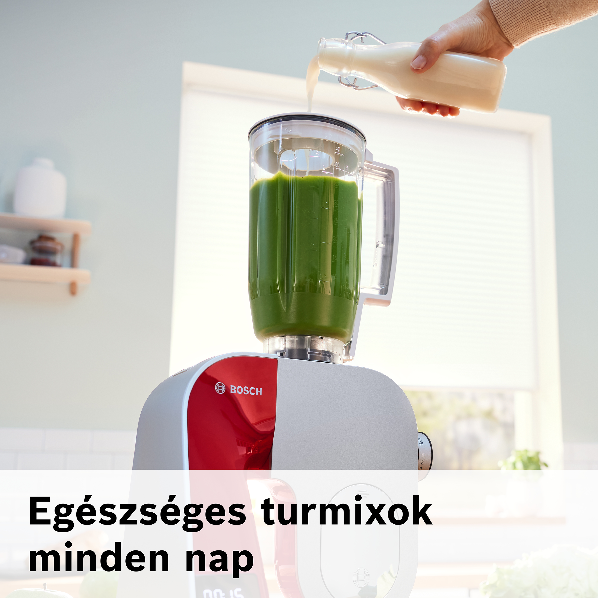 Egy személy folyadékot önt egy üvegből egy zöld tartalmú turmixgépbe. A turmixgép piros-fehér alapon áll.
