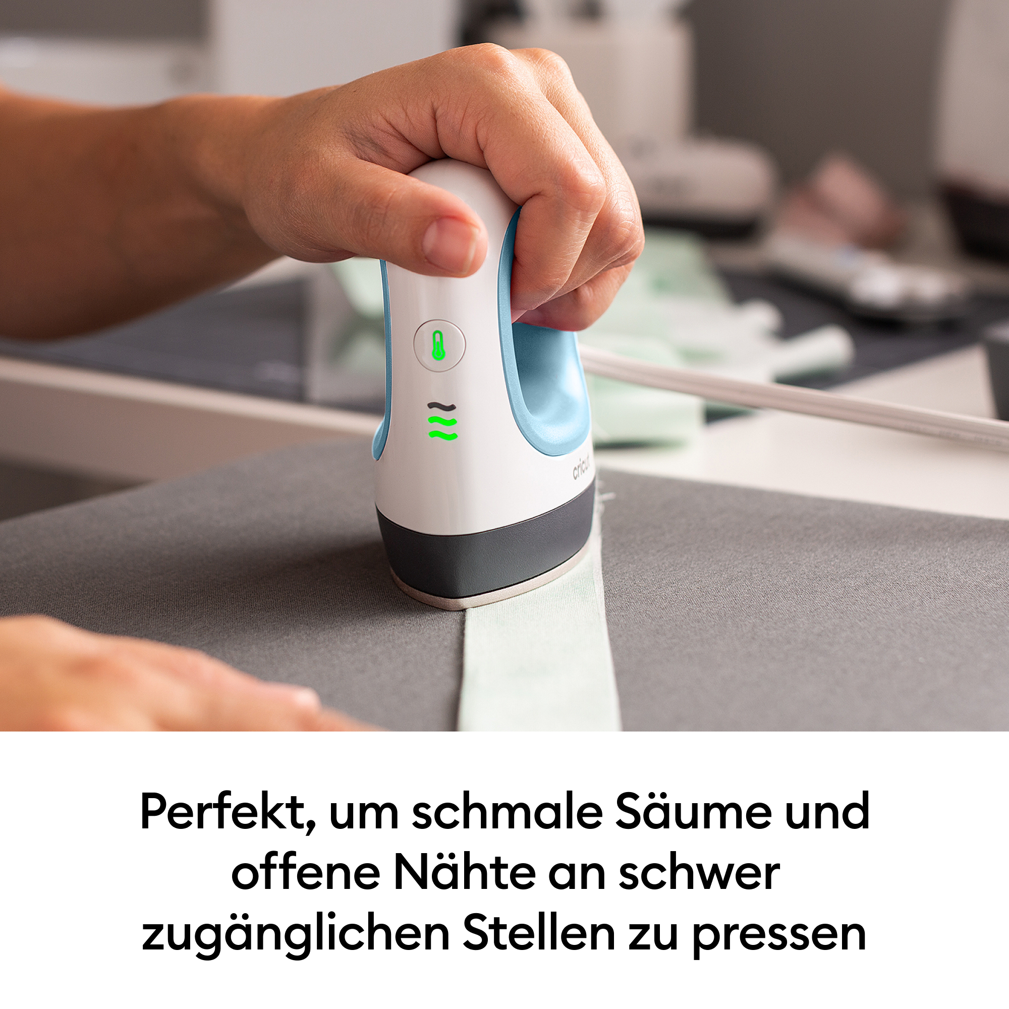 Eine Hand hält ein kleines blau-weißes Bügeleisen über Stoff auf einer grauen Oberfläche.
