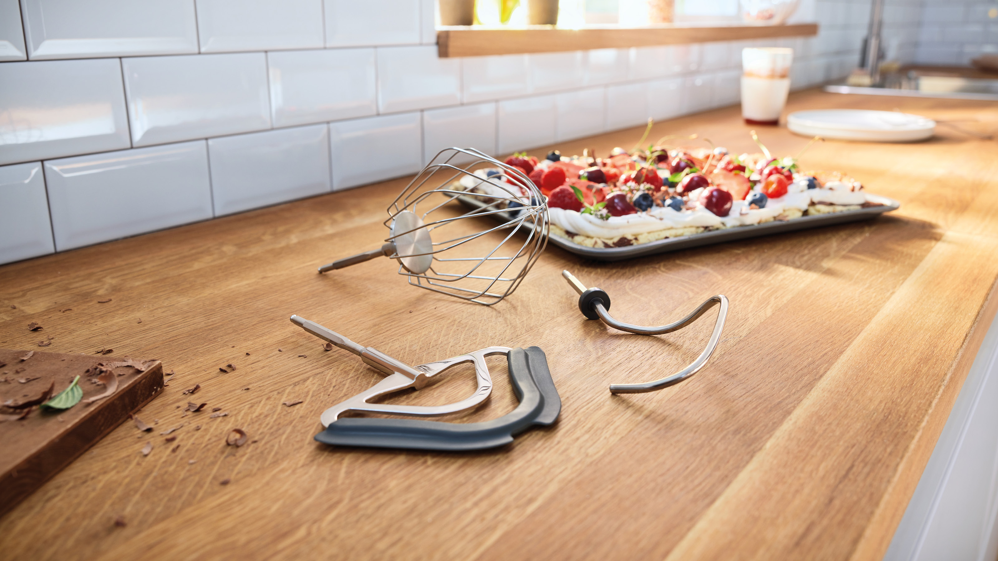 Küchenszene mit Mixer-Teilen, Dessert mit Beeren und weißen Fliesen. Holz-Arbeitsplatte.