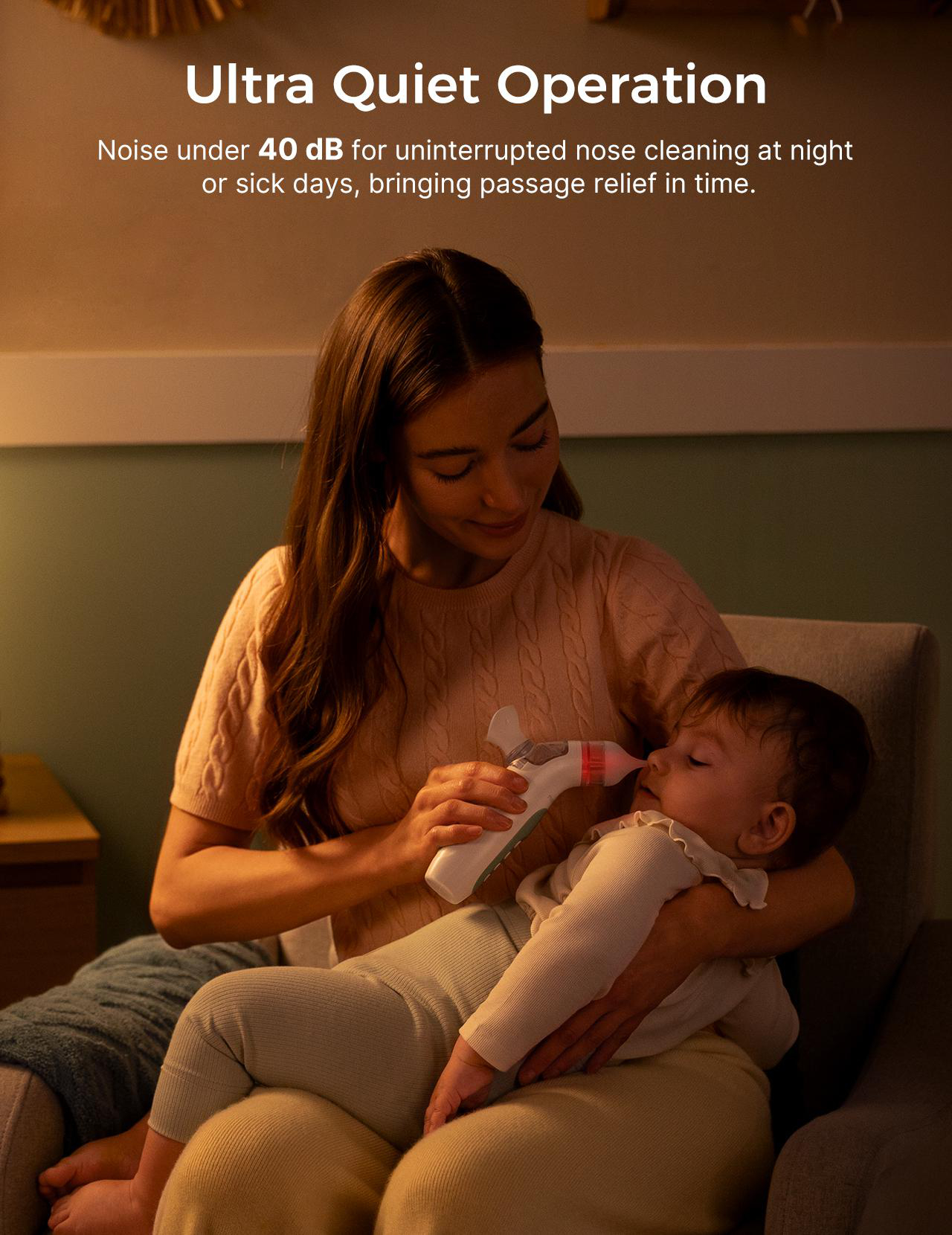 Eine Frau hält ein Baby und benutzt ein Gerät, um die Nase des Babys zu reinigen. Die Szene spielt drinnen. Beide sitzen in einem Stuhl.