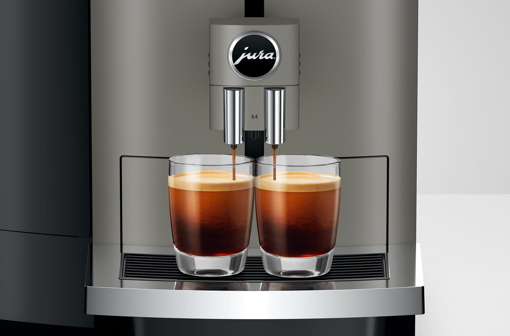 Macchina da caffè che eroga due espressi in bicchieri trasparenti. La macchina è grigia, marca Jura. Il caffè è marrone scuro.