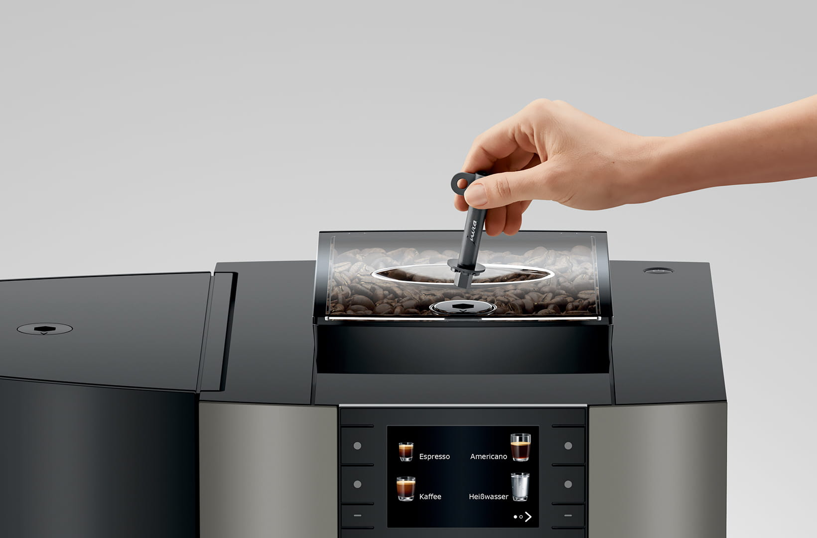 Una mano posiziona uno strumento nero nel contenitore dei chicchi di una macchina da caffè. La macchina ha un display digitale.