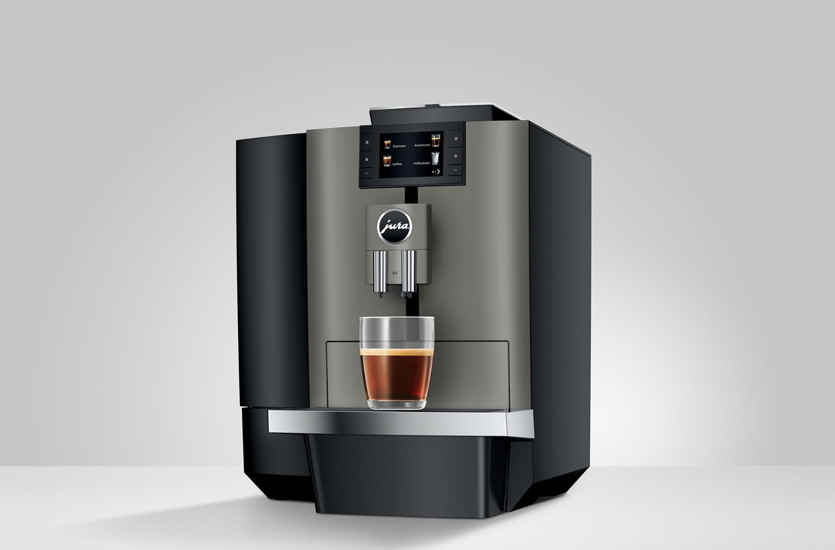 Una macchina da caffè Jura con un bicchiere di caffè è su una superficie bianca. La macchina è grigia e nera.