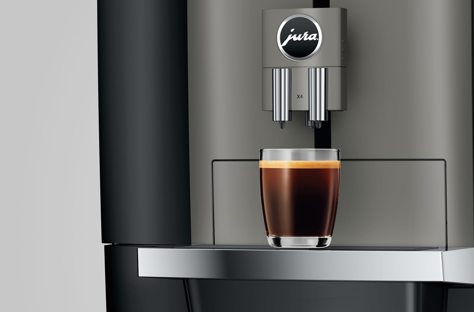 Macchina da caffè con un bicchiere di caffè. La macchina è grigia, il caffè è scuro. Il logo 'jura' è visibile.
