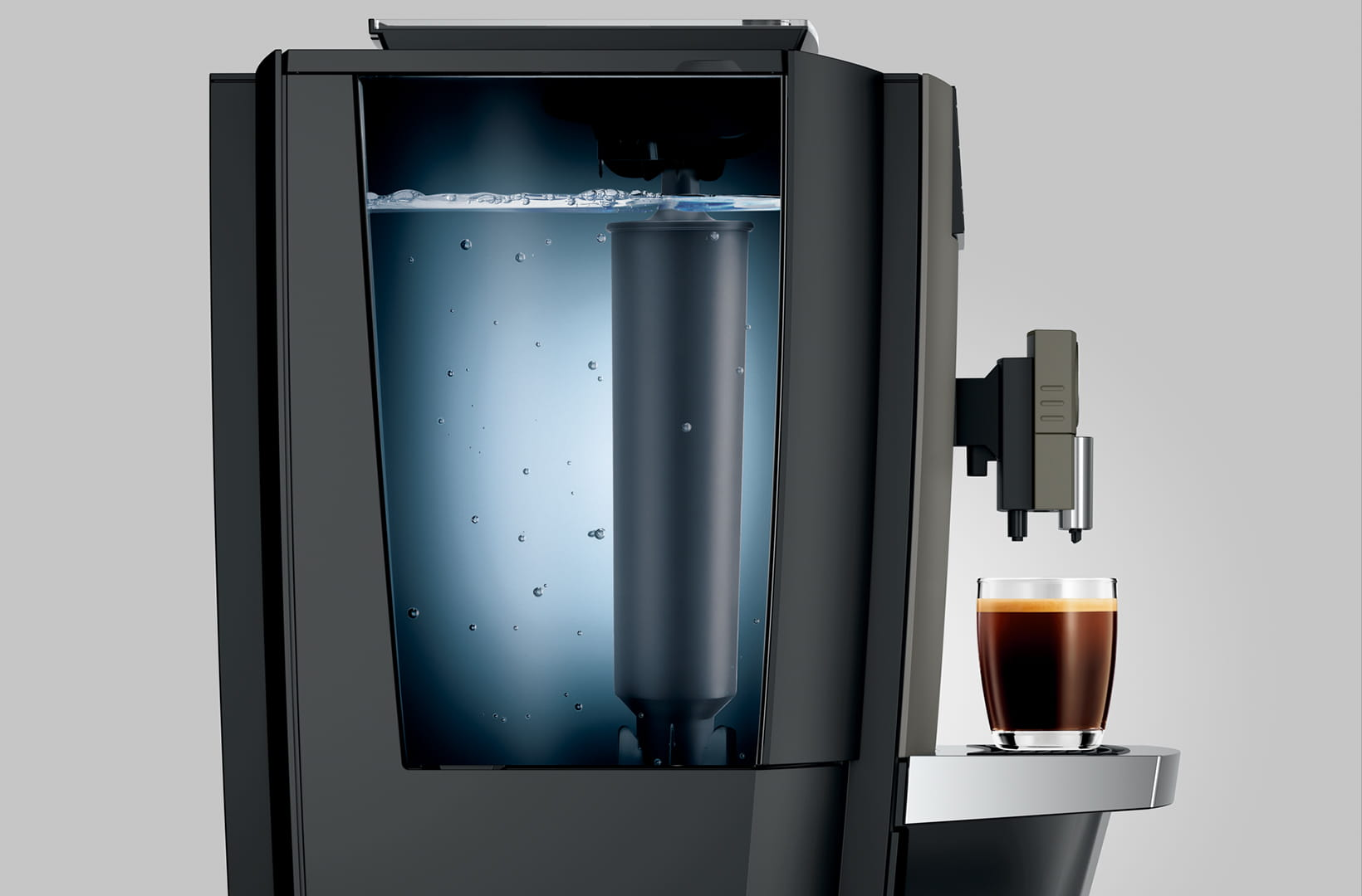 Macchina da caffè con serbatoio dell'acqua che mostra il filtro. Un bicchiere di caffè sotto l'erogatore. Macchina nera su sfondo grigio.