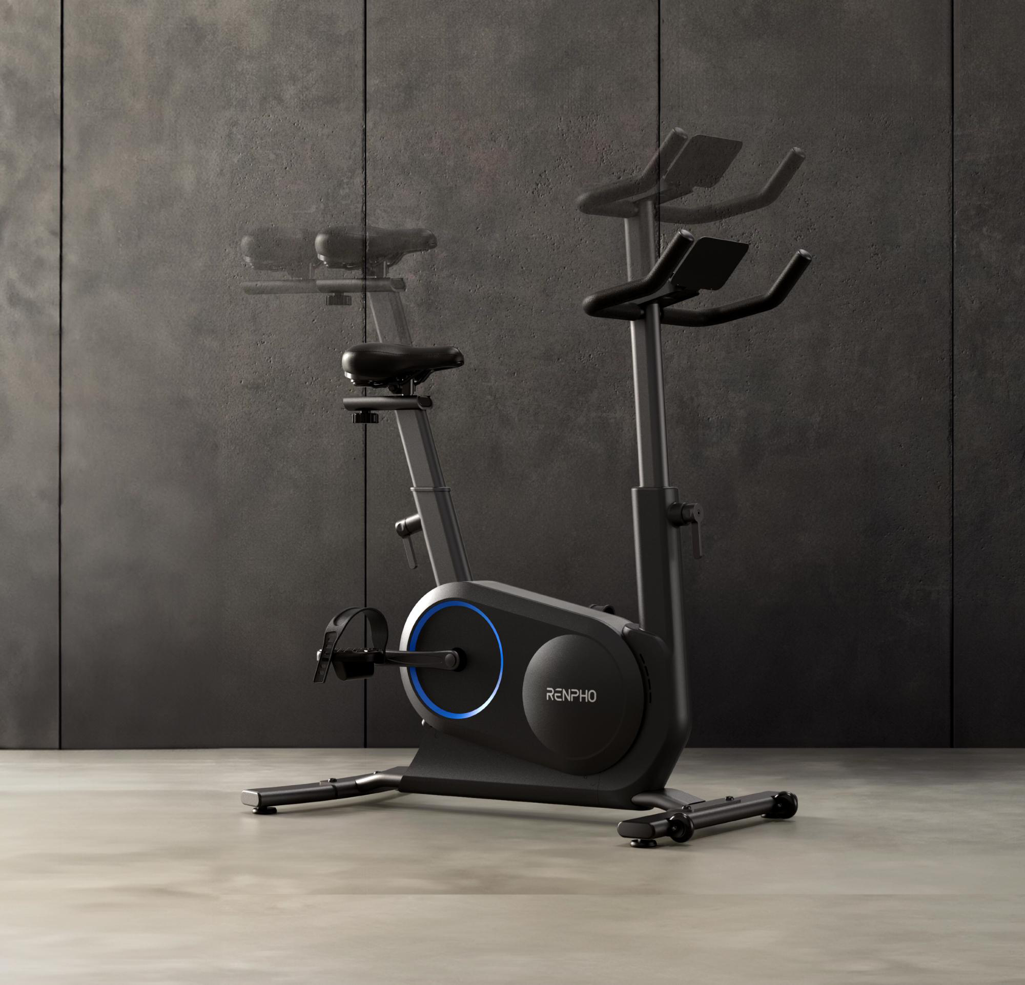 Schwarzes stationäres Fahrrad auf grauem Betonboden, mit einer dunkelgrauen Wand im Hintergrund. Das Fahrrad hat einen blauen Ring.