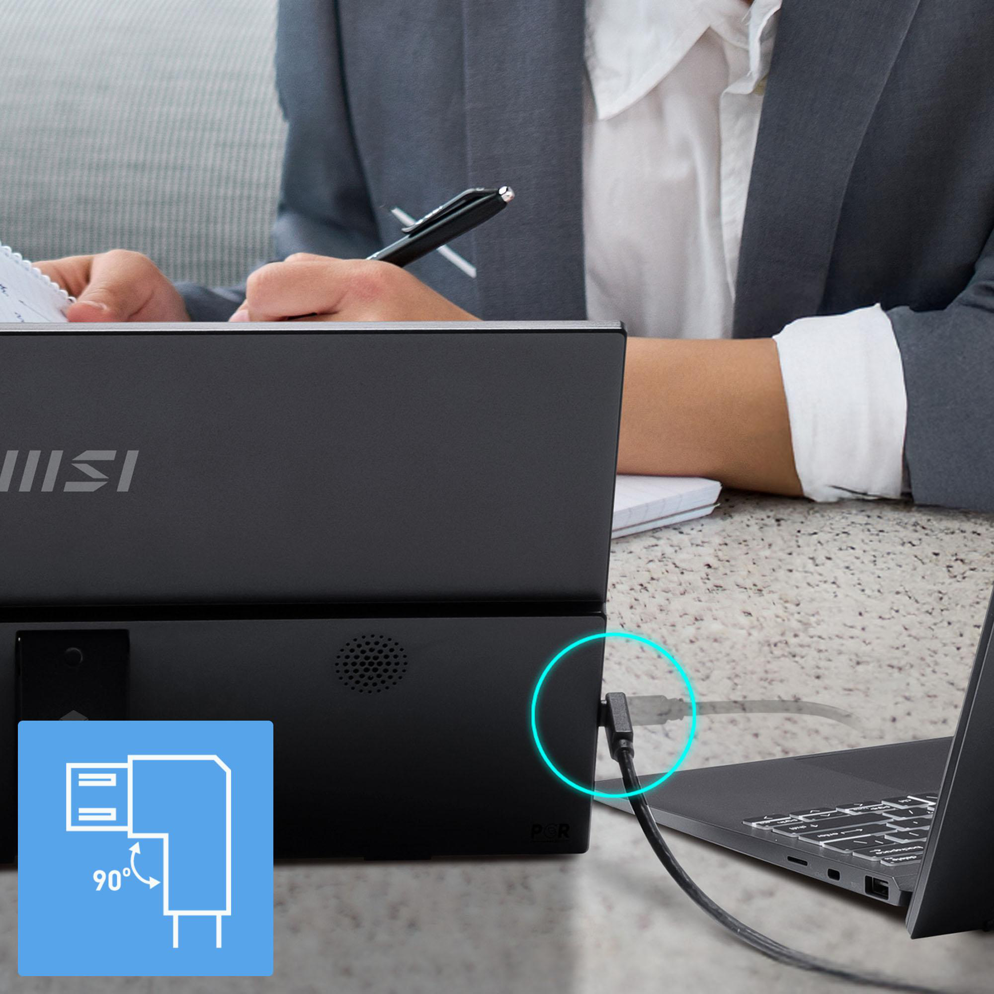 Eine Person im Anzug arbeitet mit einem Laptop, der an einen schwarzen Monitor angeschlossen ist. Ein Kabel ist in einem 90-Grad-Winkel eingesteckt.