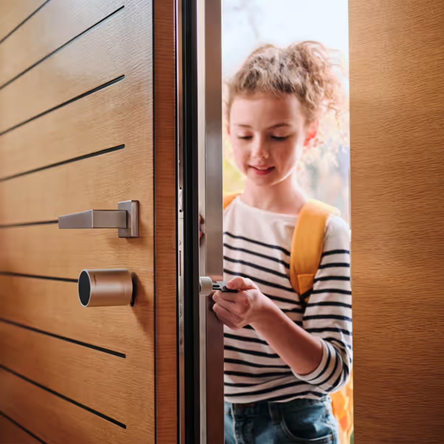 Una ragazza apre una porta di legno. Indossa una maglietta a righe e ha uno zaino. La porta ha una maniglia e una serratura.